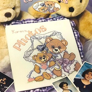 May include: Cross stitch pattern featuring two teddy bears holding an umbrella with the text "Karen's Photos" on a white background. The pattern is designed for a memory book with a size of 9 inches by 9 inches. The design size is 8.4 inches by 8.3 inches.