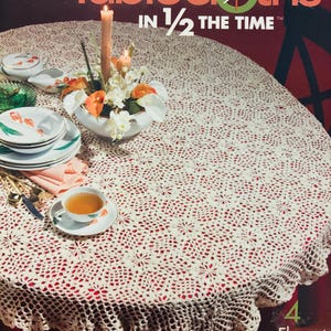 May include: A book cover for a crochet tablecloth pattern book. The cover features a white crocheted tablecloth on a red table with a floral centrepiece and candles. The title of the book is "Tablecloths in 1/2 the Time" and the author is Joyce Nordstrom.