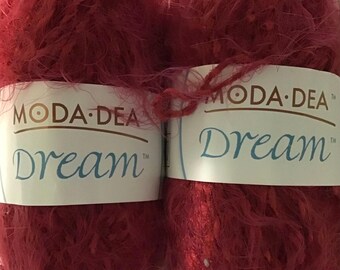 Può includere: Due gomitoli di filato Moda Dea Dream di colore rosso scuro. Il filato ha una consistenza soffice e soffice.