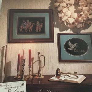 Puede incluir: Un libro titulado "And The Angels Sang" con una etiqueta de Stoney Creek Collection. El libro est&aacute; abierto y encima hay una trompeta dorada. Hay tres candelabros con velas rojas y rosas sobre una mesa de madera. Una imagen de punto de cruz enmarcada de los tres reyes magos montando camellos est&aacute; en la pared. Una imagen de punto de cruz enmarcada de una paloma con la palabra "Paz" est&aacute; en la pared. Una corona hecha de papel blanco est&aacute; en la pared.