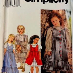 Puede incluir: Patrón de costura Simplicity para vestidos de niña. El patrón muestra ilustraciones de diferentes estilos de vestidos, incluyendo un vestido azul abotonado, un vestido rojo y un vestido a cuadros con dobladillo con volantes.