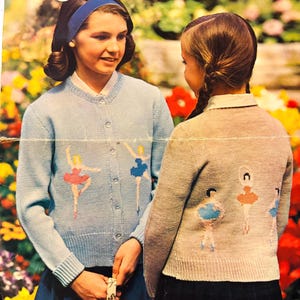 May include: Vintage knitting pattern cover showing two girls in light blue and grey cardigans, each adorned with ballerina motifs. The cover displays "Mary Maxim" and "No. 1603". A vibrant floral backdrop completes the design.