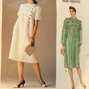 Pode incluir: Padrão de costura Vogue Patterns Paris Original n.º 1172 de Pierre Balmain. O padrão apresenta dois designs de vestidos: um vestido branco com fecho de botões e um vestido verde com riscas e mangas compridas.