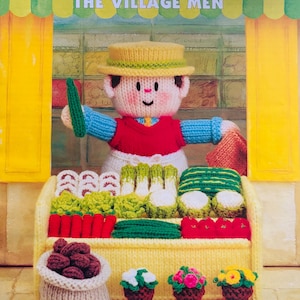 May include: A knitted doll in a yellow hat and red vest stands behind a knitted market stall filled with knitted produce. The text "Jean Greenhowe's Little Dumpling Dolls" and "Double Knitting Yarn" are visible.