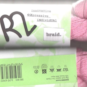 Pode incluir: Fio de lã rosa com um rótulo que diz "Innovative, Expressive, Individual, braid." O rótulo também tem um código de barras e instruções de lavagem.