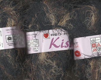 以下が含まれることがあります： 黒と茶色の糸の玉で、ラベルには「Red Heart Kiss Knit」と書いてあります。ラベルには、お手入れ方法と Coats & Clark のロゴも記載されています。