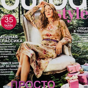 May include: The Burda Style magazine cover shows a woman in a floral dress seated in a chair. The magazine cover has the text "burda style" in large letters, with additional text in Russian. Pink gift boxes are stacked on a table.