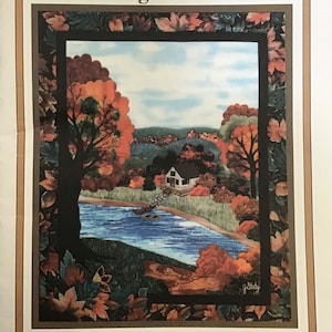 Op de afbeelding: Een ingelijst kunstwerk getiteld "A Change of Seasons" van Joan's Own Creations. De afbeelding toont een sereen herfstlandschap met een huis, een rivier en bomen met oranje en rode bladeren. Onderdeel van de Applique Series 120.