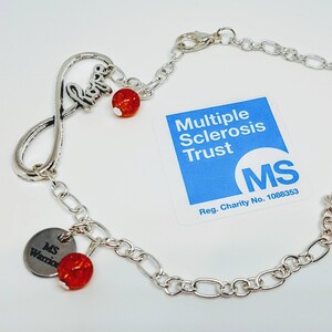 May include: Silver infinity charm bracelet with red beads and a charm that says "MS Warrior". The bracelet is accompanied by a blue card with the text "Multiple Sclerosis Trust" and the logo "MS".