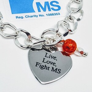 May include: Silver charm bracelet with a heart-shaped charm that says "Live, Love, Fight MS". The bracelet also has a small orange bead and a clear crystal bead.