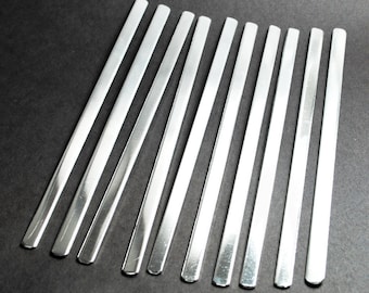 Puede incluir: Un conjunto de diez tiras de metal plateado, dispuestas en forma de abanico sobre un fondo negro. Las tiras son todas del mismo tamaño y forma, y tienen un acabado liso y brillante.