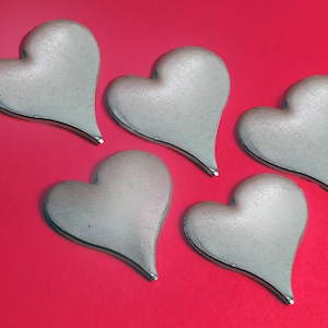 May include: Five silver-colored heart-shaped objects with a metallic sheen are arranged on a vibrant red background. Each heart has a smooth, rounded form with a pointed bottom. The hearts are evenly spaced, creating a visually appealing pattern.