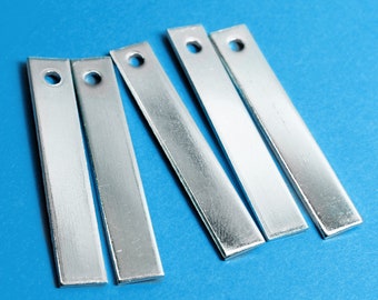 Puede incluir: Cinco tiras de metal plateado con un agujero en el centro de cada tira. Las tiras están dispuestas en una fila, con los extremos de las tiras superpuestos.