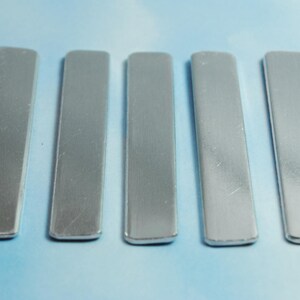 May include: Five silver metal bars, each with a smooth, slightly textured surface. The bars are arranged horizontally in a row, with the ends of each bar slightly rounded.