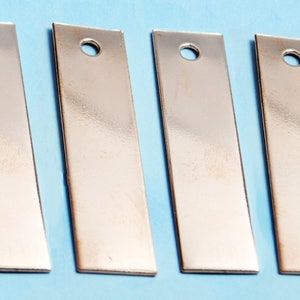 May include: Six silver-colored metal tags with a hole in the top. The tags are rectangular and have a slightly curved shape.