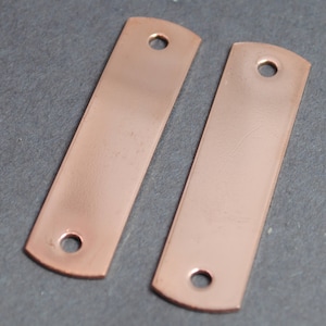 May include: Two rectangular copper-colored metal tags with rounded edges and a hole at each end.