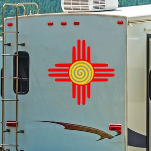 May include: A white camper van with a red and yellow Zia symbol on the side. The camper has a ladder on the side and a window on the back.