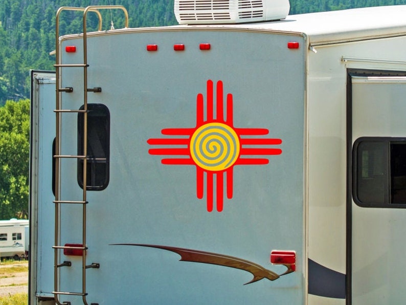 May include: A white camper van with a red and yellow Zia symbol on the side. The camper has a ladder on the side and a window on the back.