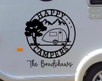 May include: A black circular vinyl decal applied to a light-colored vehicle surface. The design features a teardrop camper, a tree, and mountain silhouettes with the text HAPPY CAMPERS in a circular border and The Bradshaws below.