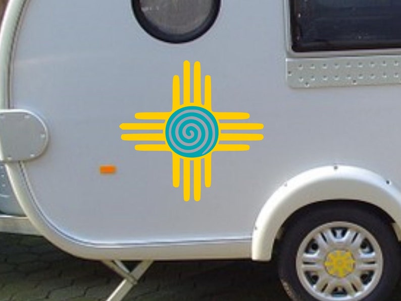 May include: A white camper van with a yellow and blue stylized symbol of a spiral inside a circle with four arms extending out from the circle. The symbol is commonly known as the "Sun Symbol" or "Southwest Symbol".