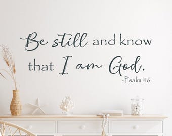 May include: A black wall decal featuring the script and serif text Be still and know that I am God. Psalm 46. The lettering is displayed in a two-line arrangement with a decorative font style, positioned against a plain white background.