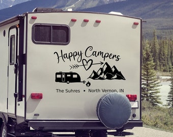 以下が含まれることがあります： 白いキャンピングカーに、「Happy Campers」という黒いステッカーが貼られています。ステッカーには、ハート、矢印、山、キャンピングカーが描かれており、「The Suhres - North Vernon, IN」というテキストも含まれています。