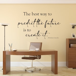 May include: A motivational quote by Abraham Lincoln on a beige wall in a home office setting. The quote reads: "The best way to predict the future is to create it." -Abraham Lincoln