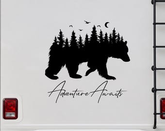 May include: A black vinyl decal applied to a white vehicle surface, featuring a silhouette of a walking bear with a forest of pine trees inside its body, a crescent moon, and birds above, with the text Adventure Awaits written below.