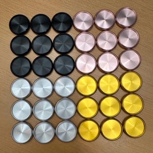 May include: A collection of 36 round, flat, decorative buttons in various colors. The buttons are arranged in four rows of nine buttons each. The first row features black buttons, the second row features silver buttons, the third row features gold buttons, and the fourth row features pink buttons.