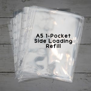 Può includere: Una pila di ricariche A5 trasparenti a caricamento laterale. Il testo "A5 1-Pocket Side Loading Refill" è stampato in nero. Le pagine sono realizzate in materiale trasparente e hanno fori per la rilegatura.