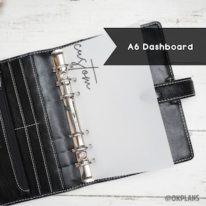 May include: A black leather A6 binder with a white page inside. The page has the word "custom" written on it. The binder has a silver ring mechanism.