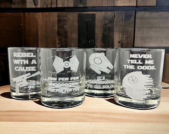 May include: Four clear glass tumblers with Star Wars themed etchings. The tumblers feature the Millennium Falcon, a TIE fighter, a Death Star, and a blaster. The text on the tumblers reads "Rebel with a Cause", "Pew Pew Pew Whoooosh Pew Pew Pew", "It's Dangerous to Go Solo", and "Never Tell Me the Odds."