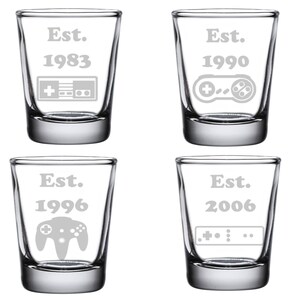 May include: Four clear glass shot glasses with etched designs. Each glass features a different year, from 1983 to 2006, and a retro video game controller. The text "Est." is above each year.