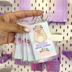 Puede incluir: Un conjunto de tarjetas laminadas con un dibujo de una llama con una corona de flores. Las tarjetas muestran el nombre "Elianys Santiago Rodriguez" y el texto "Mis Tablas de Multiplicar". Las tarjetas están unidas con una cadena.