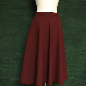 May include: A maroon midi skirt with a flared silhouette. The skirt is made of a smooth, woven fabric and has a simple, fitted waistband.