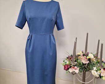 May include: A blue knee-length dress with short sleeves and a round neckline. The dress is on a mannequin in front of a white wall. The text "Natalija Jershova" is visible above the mannequin.