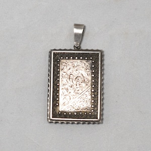 May include: A silver pendant with a rectangular design. The pendant features a detailed, intricate floral pattern and a geometric pattern in the centre.