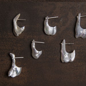 May include: Five pairs of white pearl earrings with silver posts. The earrings are all different shapes and sizes.