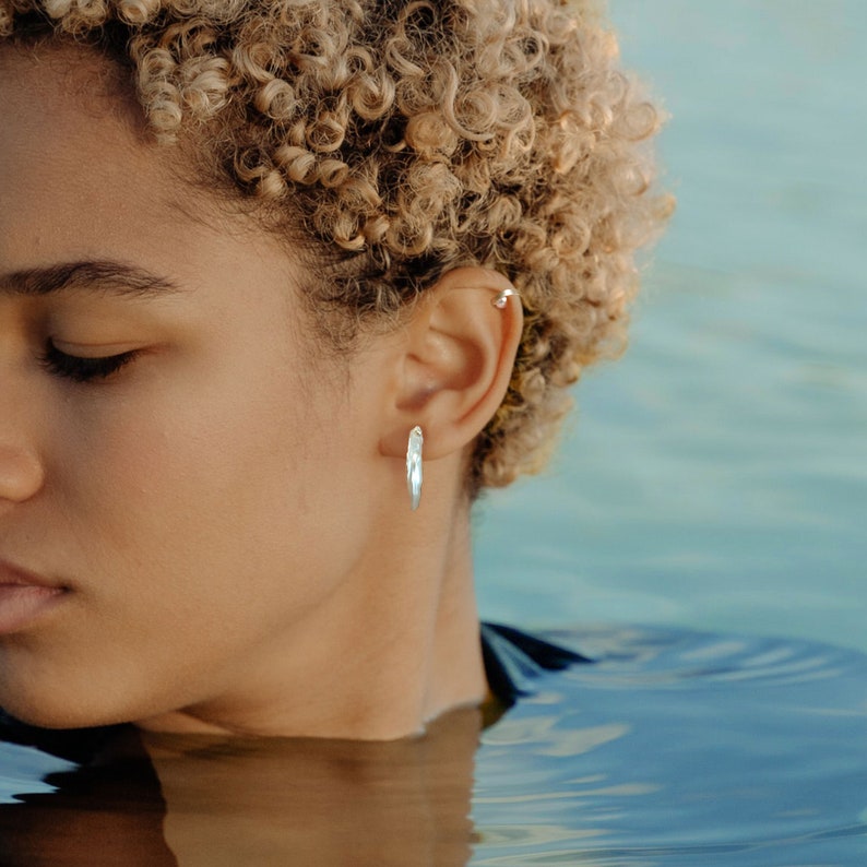 May include: A person with curly blonde hair wearing a silver hoop earring. The person is partially submerged in water.