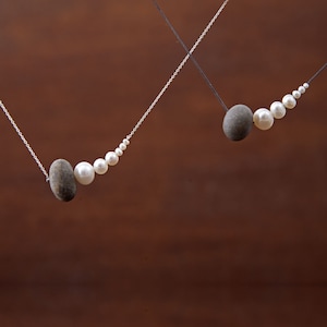 May include: Two necklaces with silver chains and white pearls. One necklace has a larger grey stone at the end, the other has a smaller grey stone.