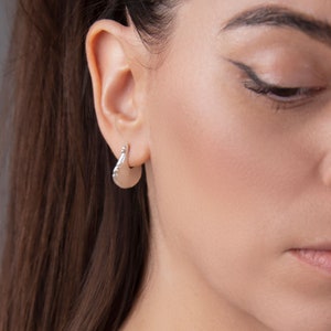May include: Silver hoop earrings with a slightly curved, half-circle shape. The earrings have a smooth, polished finish.