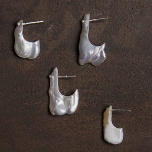 May include: Four pairs of white pearl earrings with silver hoops. The earrings are of different sizes and shapes.