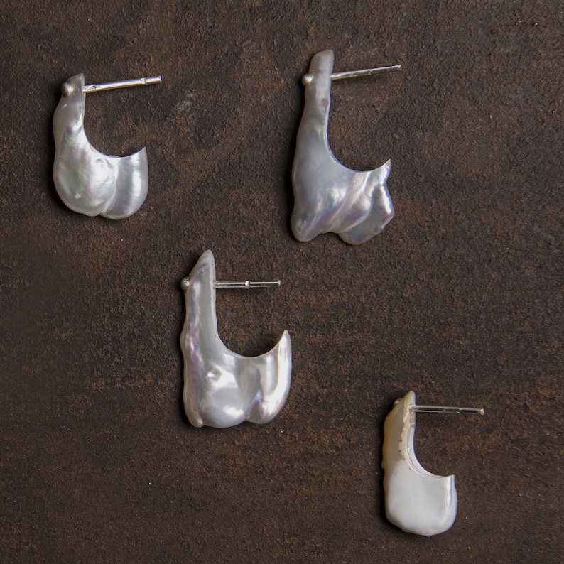 May include: Four pairs of white pearl earrings with silver hoops. The earrings are of different sizes and shapes.