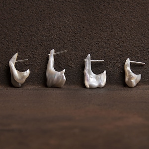 May include: Four white pearl earrings with silver posts. The earrings are shaped like irregular, organic forms.