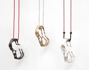 Può includere: Tre collane con ciondoli astratti in nero, oro e argento, ciascuna sospesa da un cordino. I ciondoli hanno un design aperto unico, con la collana nera appesa a un cordino rosso.