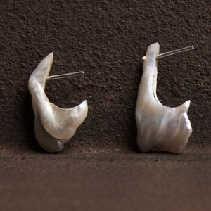 May include: A pair of white pearl earrings with a unique, irregular shape. The earrings are attached to silver posts.