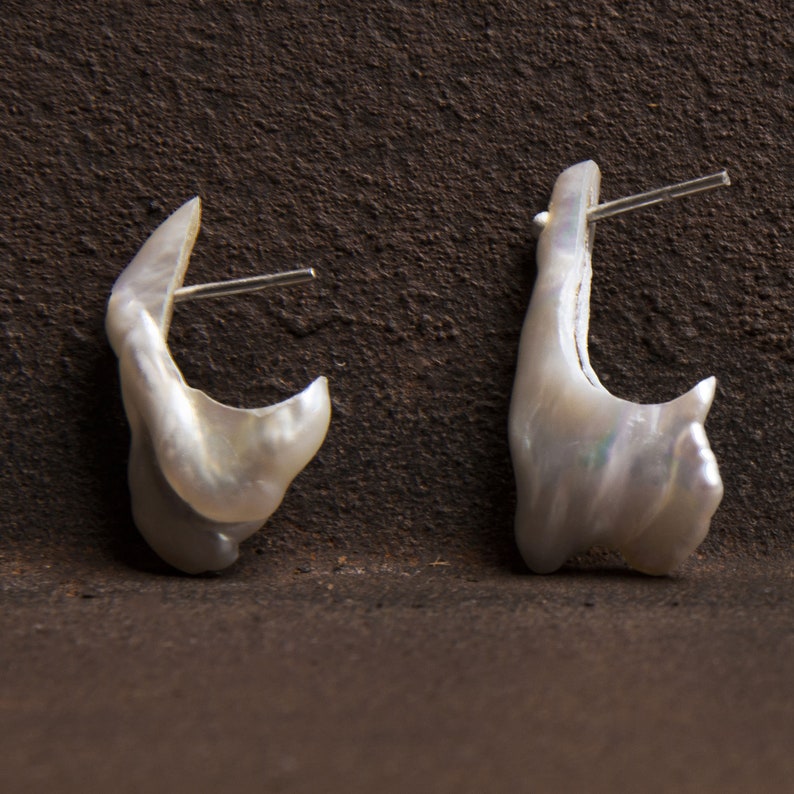 May include: A pair of white pearl earrings with a unique, irregular shape. The earrings are attached to silver posts.