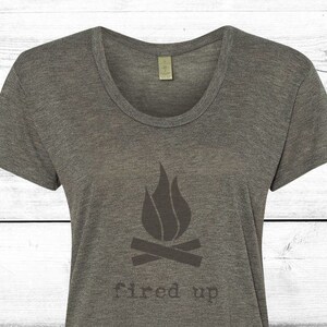 Puede incluir: Camiseta gris jaspeado con cuello redondo y un gr&aacute;fico gris oscuro de una fogata con llamas y las palabras "fired up" impresas debajo. La camiseta est&aacute; hecha de un material suave.