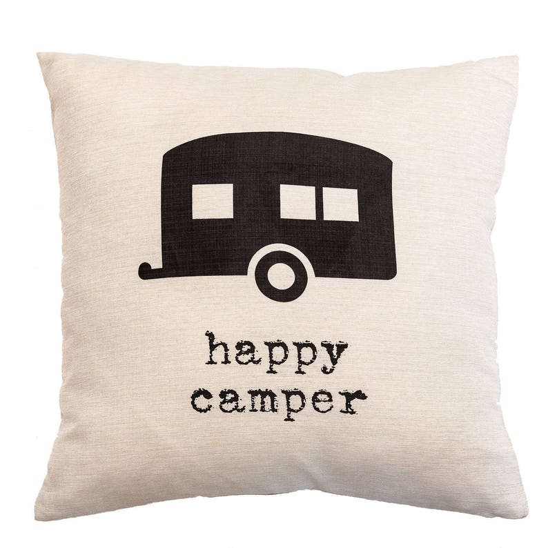 May include: A square, off-white pillow with a black graphic of a camper and the words "happy camper" printed below. The camper has two square windows and one rectangular window. The pillow has a textured appearance.