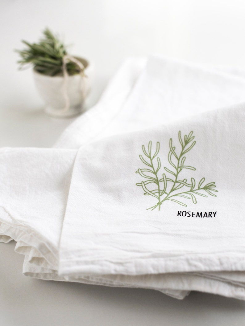 May include: White kitchen towel with a green rosemary sprig illustration and the word "ROSEMARY" printed below. A small white bowl with rosemary sprigs is in the background.